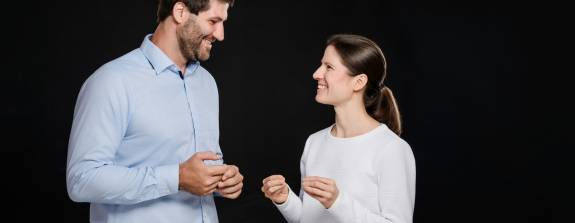 Priv.-Doz. Dr. med. Katharina Lechner und Dr. med. Benjamin Lechner stehen sich lächelnd gegenüber und unterhalten sich vor schwarzem Hintergrund.