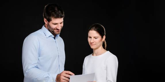 Priv.-Doz. Dr. med. Katharina Lechner und Dr. med. Benjamin Lechner betrachten gemeinsam ein Dokument vor schwarzem Hintergrund.
