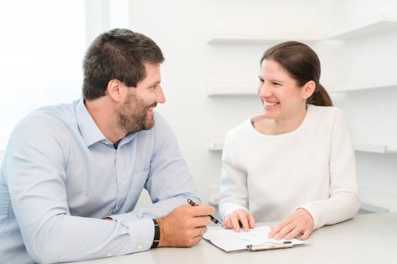 Priv.-Doz. Dr. med. Katharina Lechner und Dr. med. Benjamin Lechner sitzen lächelnd an einem Tisch und besprechen gemeinsam Unterlagen.
